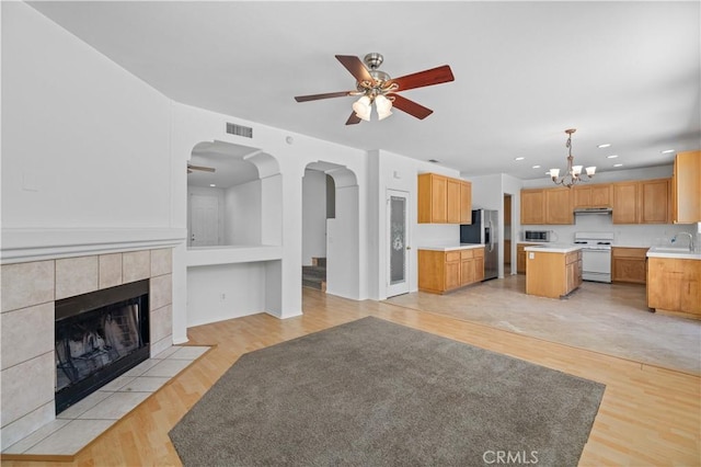 unfurnished living room featuring a ceiling fan, a chandelier, a sink, arched walkways, and light wood finished floors