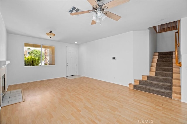 unfurnished living room with stairs, wood finished floors, ceiling fan, and a tile fireplace
