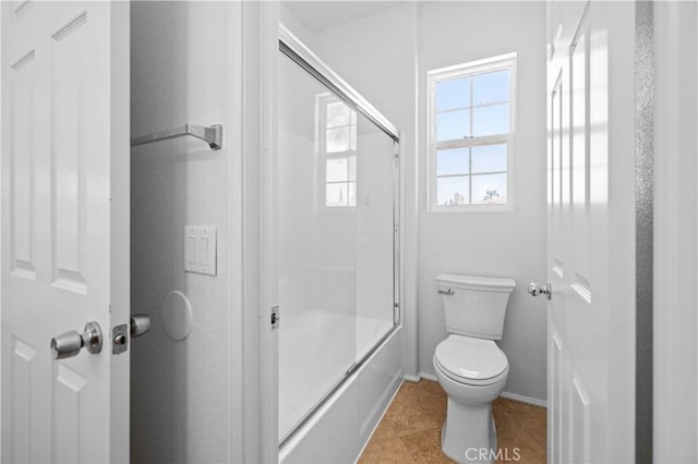 bathroom with toilet, baseboards, and shower / bath combination with glass door