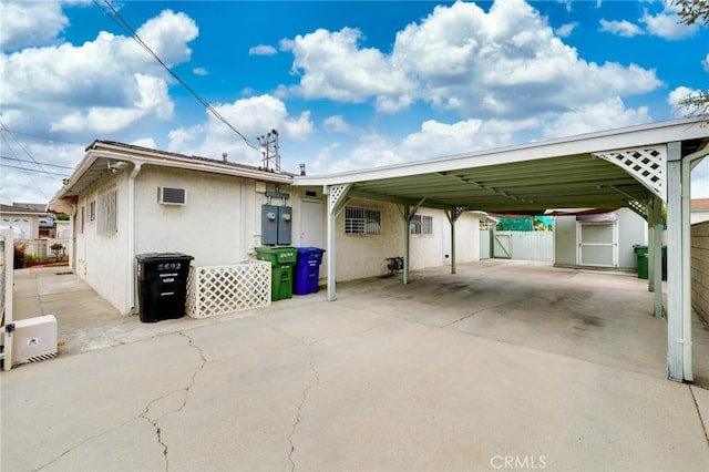 rear view of house with a shed, a carport, fence, an outbuilding, and stucco siding