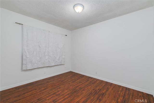 spare room with wood finished floors, a textured ceiling, and baseboards