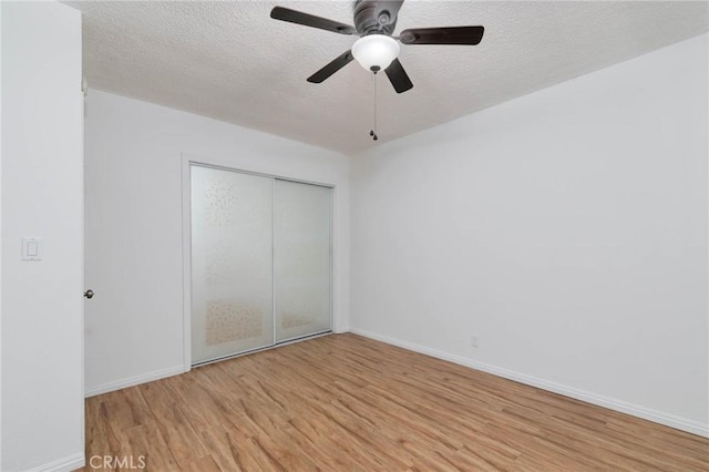 unfurnished bedroom with light wood-style flooring, a textured ceiling, baseboards, a closet, and a ceiling fan