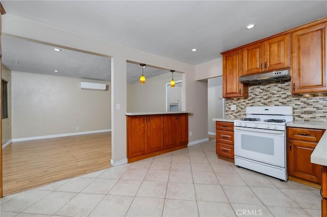 kitchen with white gas range oven, under cabinet range hood, brown cabinets, backsplash, and light countertops
