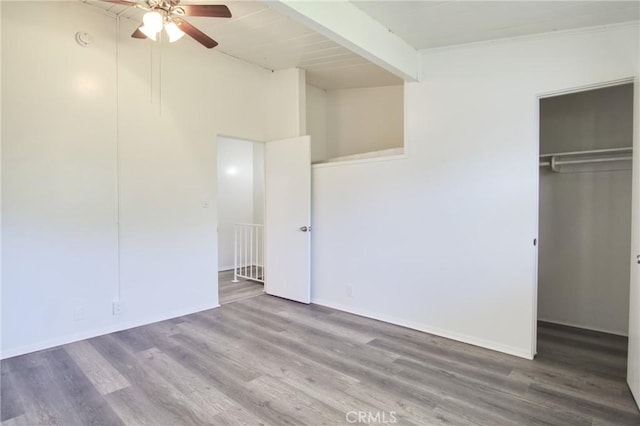 unfurnished bedroom featuring wood finished floors, a closet, a spacious closet, and baseboards