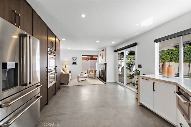 11 Bayside, Irvine, CA 92614 - kitchen featuring appliances with stainless steel finishes, recessed lighting, dark brown cabinets, a tile fireplace, and light stone counters