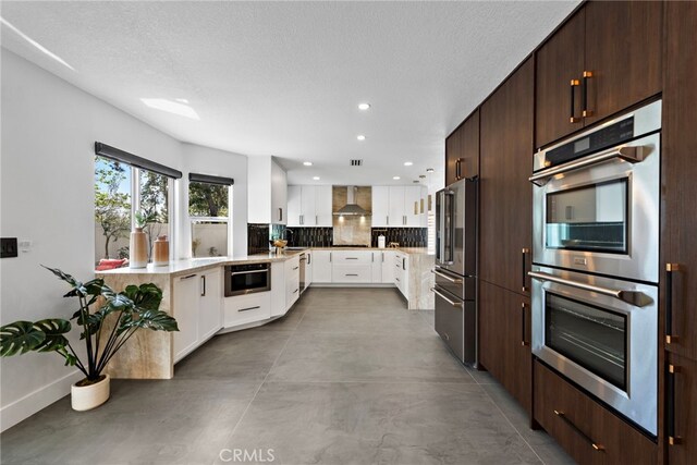 11 Bayside, Irvine, CA 92614 - kitchen with appliances with stainless steel finishes, wall chimney exhaust hood, white cabinetry, recessed lighting, and finished concrete floors