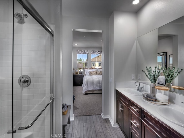 ensuite bathroom with wood finished floors, tiled shower, double vanity, baseboards, and recessed lighting