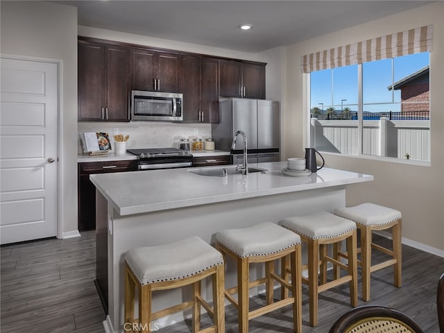 kitchen with stainless steel appliances, a sink, dark wood-type flooring, baseboards, and light countertops