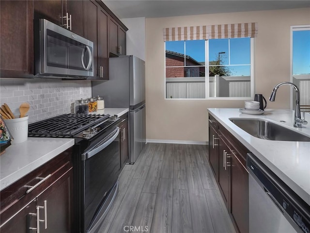 kitchen with stainless steel appliances, a sink, light wood-type flooring, baseboards, and light countertops