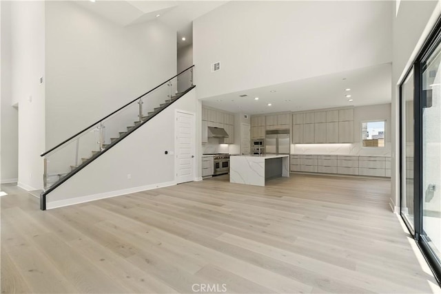 208 Stage, Irvine, CA 92618 - unfurnished living room with a towering ceiling, stairway, light wood-style floors, and recessed lighting