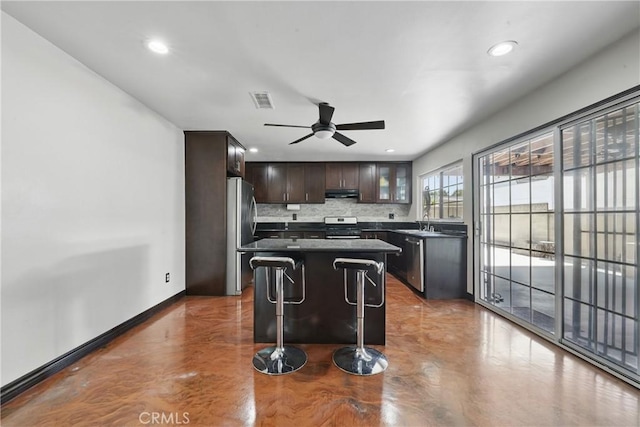kitchen featuring appliances with stainless steel finishes, under cabinet range hood, backsplash, a center island, and finished concrete floors