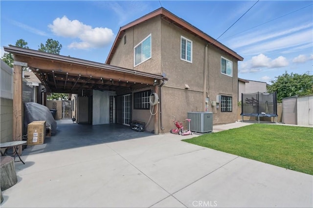 rear view of property featuring a trampoline, stucco siding, a yard, and central AC