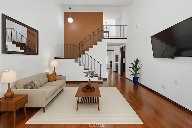 living area with a high ceiling, wood finished floors, stairs, and baseboards