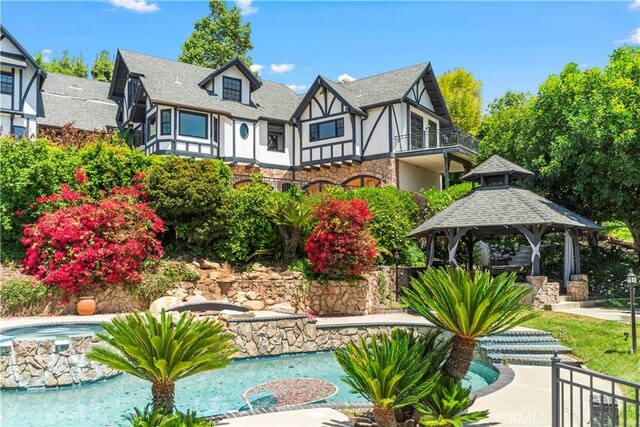 7008 Hawarden Dr, Riverside, CA 92506 - rear view of house with a gazebo, stone siding, a balcony, a pool with connected hot tub, and stucco siding