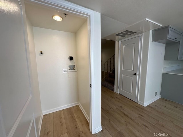 corridor with light wood-style floors, stairway, and baseboards