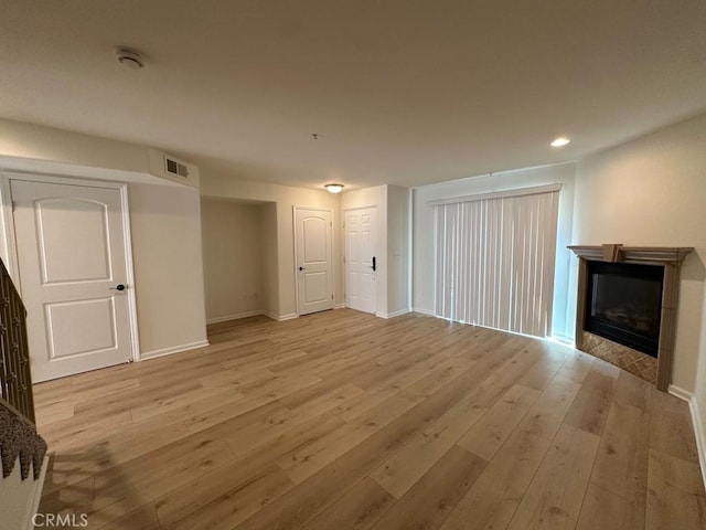 unfurnished living room featuring a glass covered fireplace, light wood-style flooring, baseboards, and recessed lighting