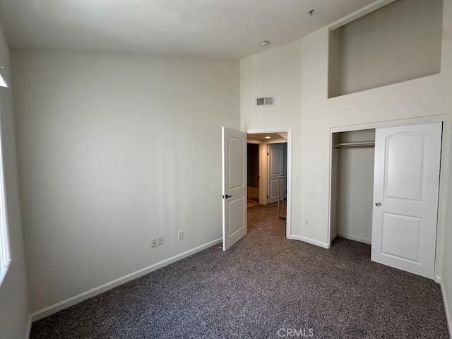 unfurnished bedroom with baseboards, dark colored carpet, a high ceiling, and a closet