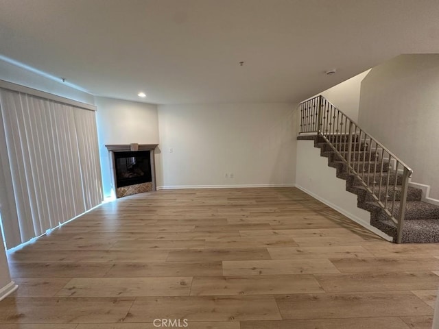 unfurnished living room with wood finished floors, stairway, recessed lighting, a glass covered fireplace, and baseboards