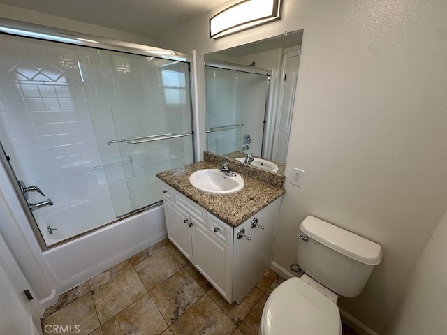 full bathroom featuring toilet, baseboards, vanity, stone finish flooring, and bath / shower combo with glass door