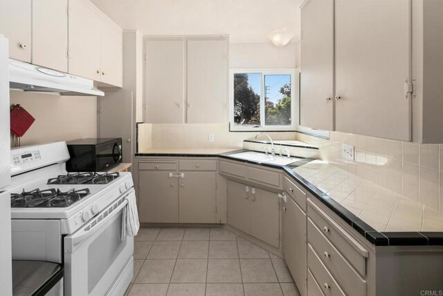 1855 Rubenstein Dr, Cardiff By The Sea, CA 92007 - kitchen with white gas stove, black microwave, a sink, tile countertops, and under cabinet range hood