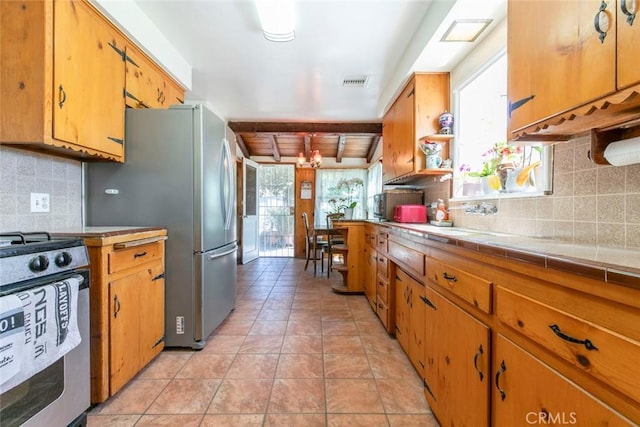 14719 Wyandotte St, Van Nuys, CA 91405 - kitchen featuring stainless steel gas stove, backsplash, tile counters, light tile patterned flooring, and brown cabinetry