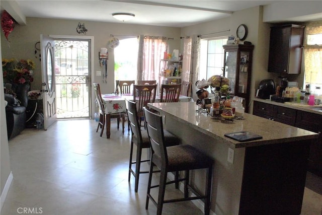 975 E Citrus St, Riverside, CA 92507 - kitchen featuring a kitchen island, a kitchen bar, dark brown cabinets, light stone countertops, and light floors