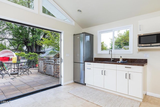 kitchen with stainless steel microwave, plenty of natural light, vaulted ceiling, white cabinetry, and baseboards