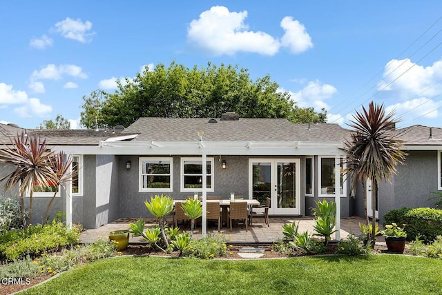 back of house with stucco siding, a lawn, and a shingled roof