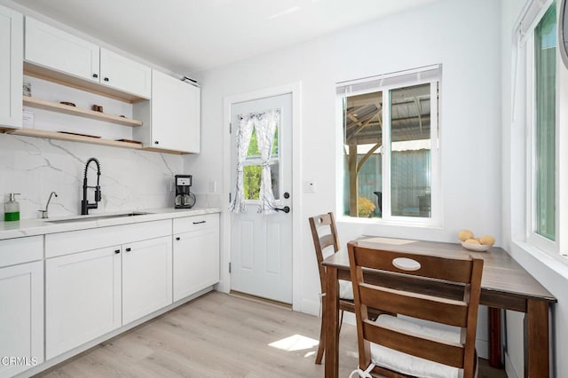 kitchen with a sink, open shelves, tasteful backsplash, light wood-type flooring, and light countertops