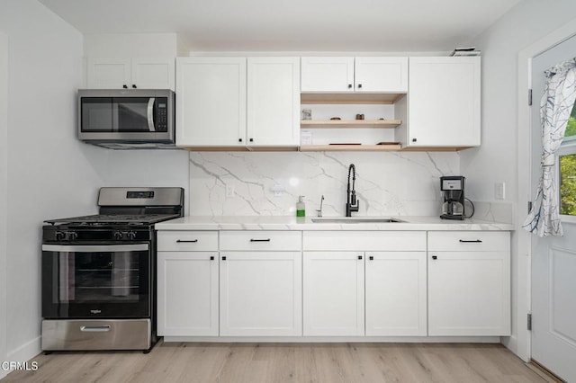 kitchen with appliances with stainless steel finishes, a sink, light wood-style floors, and white cabinets