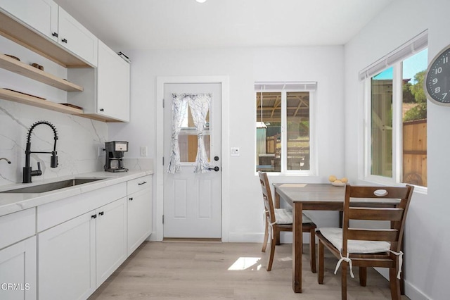 kitchen with a sink, light wood-style floors, open shelves, white cabinetry, and light countertops