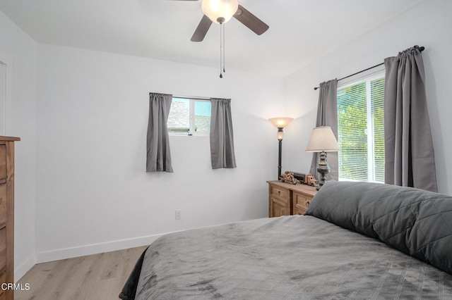 bedroom featuring wood finished floors, multiple windows, baseboards, and ceiling fan