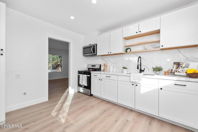 kitchen with appliances with stainless steel finishes, a sink, light wood-style flooring, white cabinets, and tasteful backsplash
