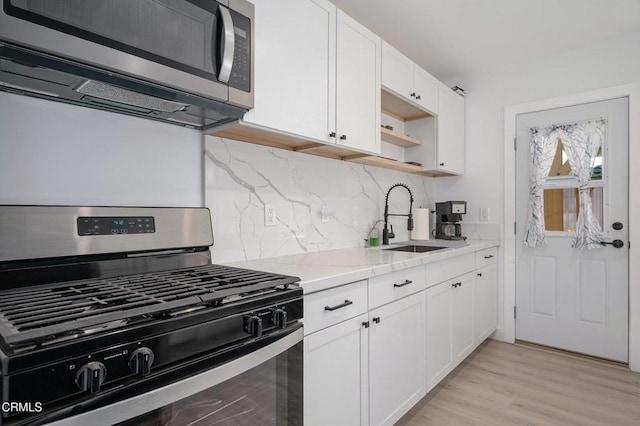 kitchen with appliances with stainless steel finishes, a sink, decorative backsplash, white cabinetry, and light wood finished floors