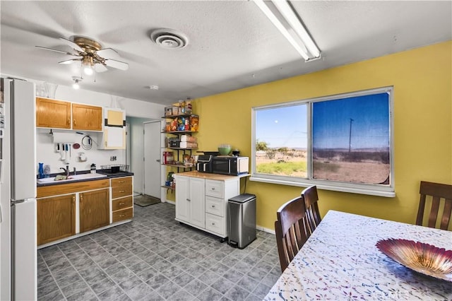 kitchen with ceiling fan, freestanding refrigerator, tile patterned floors, baseboards, and a textured ceiling