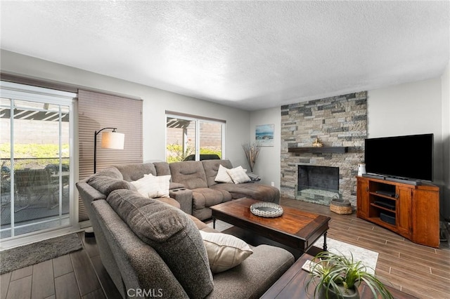 living room with wood finish floors, a textured ceiling, and a stone fireplace