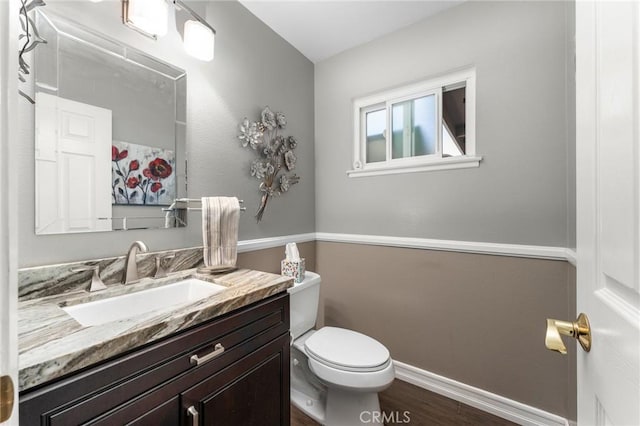 half bathroom featuring toilet, wood finished floors, vanity, and baseboards
