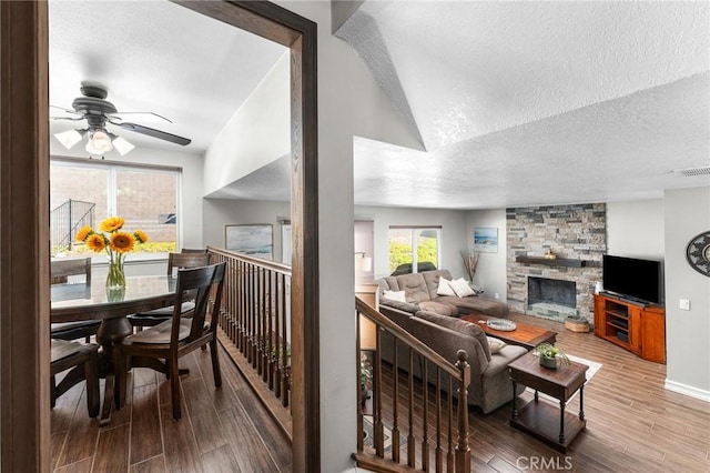 living room with wood finished floors, a textured ceiling, ceiling fan, a stone fireplace, and baseboards