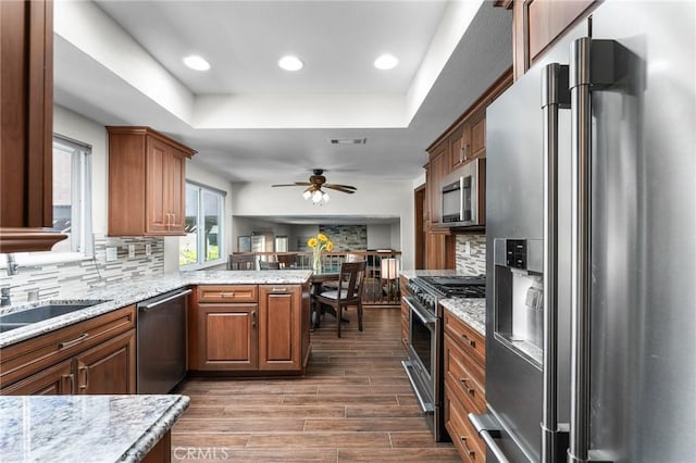 kitchen with appliances with stainless steel finishes, a tray ceiling, a peninsula, backsplash, and recessed lighting