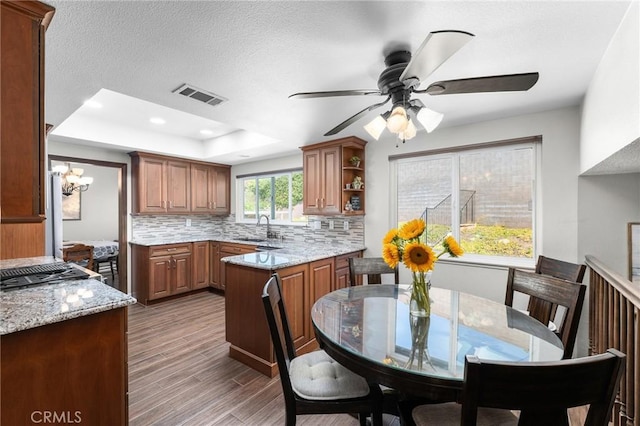 kitchen featuring a sink, a raised ceiling, decorative backsplash, light stone counters, and a peninsula