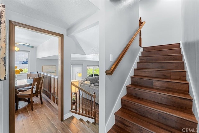 stairs featuring wood finished floors, a textured ceiling, and baseboards