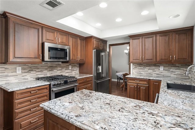kitchen featuring high end appliances, a sink, a raised ceiling, light stone countertops, and recessed lighting