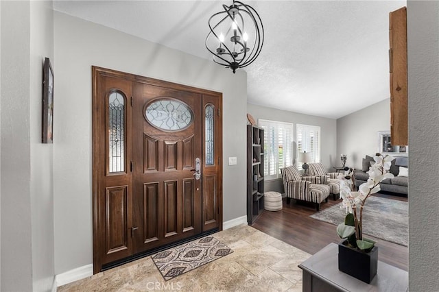 foyer entrance featuring a chandelier, baseboards, and vaulted ceiling