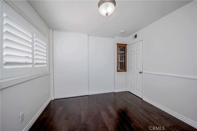 unfurnished bedroom featuring wood finished floors, baseboards, and a closet