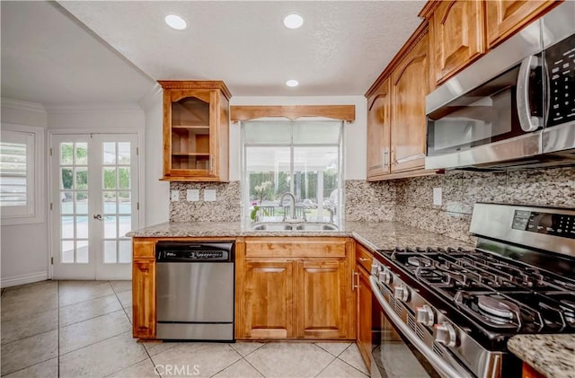 kitchen with stainless steel appliances, a sink, light stone countertops, brown cabinets, and ornamental molding