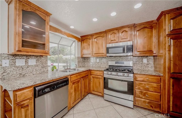 kitchen with stainless steel appliances, a sink, a textured ceiling, light tile patterned flooring, and light stone countertops