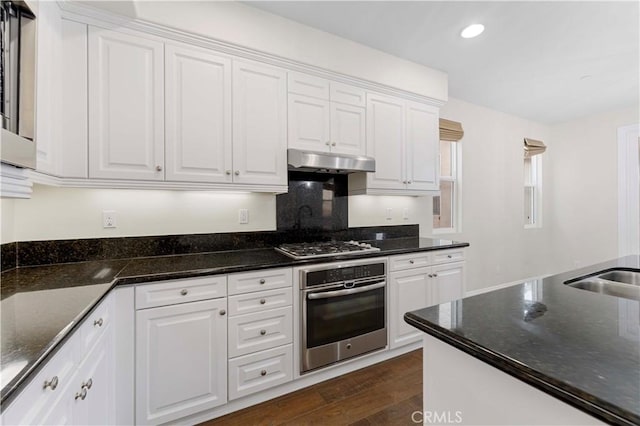 20304 Estuary Ln, Newport Beach, CA 92660 - kitchen featuring appliances with stainless steel finishes, under cabinet range hood, white cabinetry, dark wood-type flooring, and dark stone counters