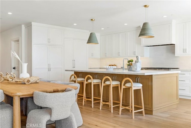 1759 Glenneyre St, Laguna Beach, CA 92651 - kitchen with light wood-style floors, a center island with sink, white cabinets, light countertops, and a kitchen breakfast bar
