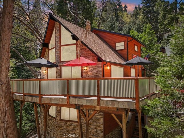 385 Iris Dr, Twin Peaks, CA 92391 - back of house at dusk with stone siding, a wooden deck, and roof with shingles