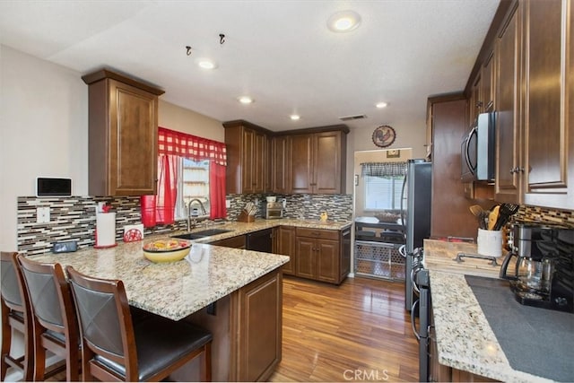 12427 Stardell Ln, Yucaipa, CA 92399 - kitchen featuring stainless steel appliances, a sink, a peninsula, light wood-style floors, and backsplash